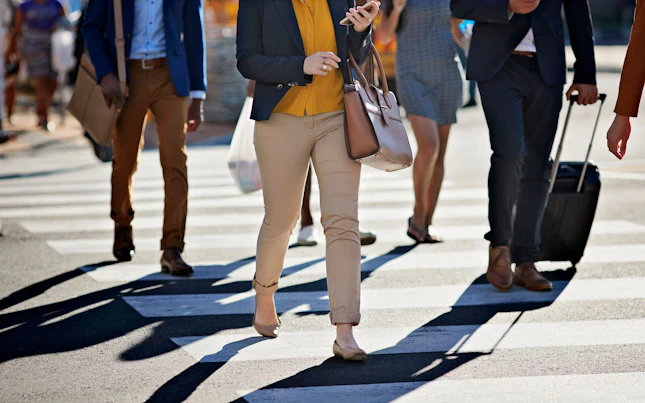 Business people walking on pedestrian crossing, with phones and bags, at sunset
